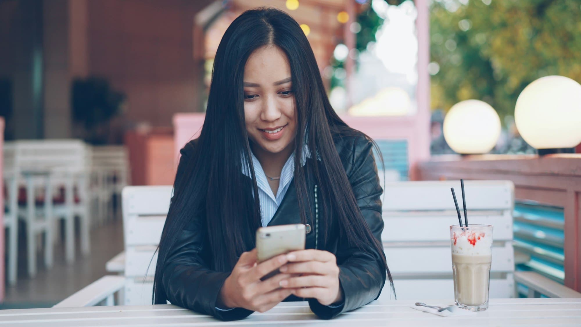 Une cliente sourit en lisant un email sur son téléphone, à la terrasse d'un café